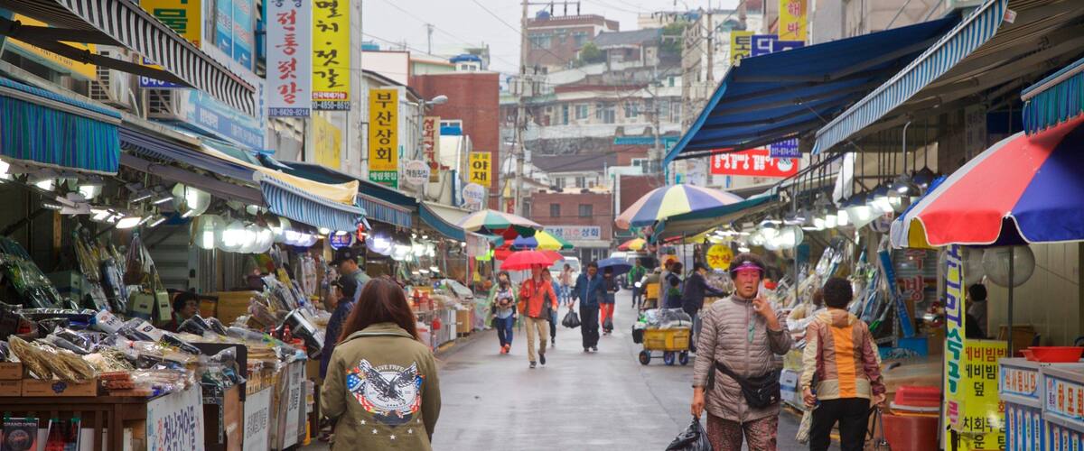 A bustling market street with various stalls and people walking.
