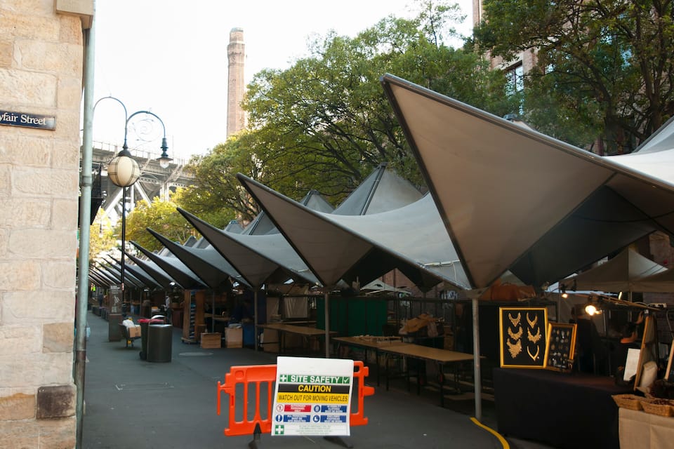A street lined with tents, a sign for 'Fair Street,' and a 'Site Safety' caution sign.