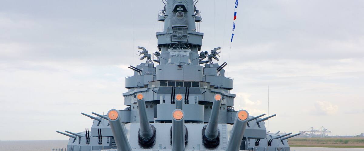 A large naval ship with multiple gun turrets and a flag.