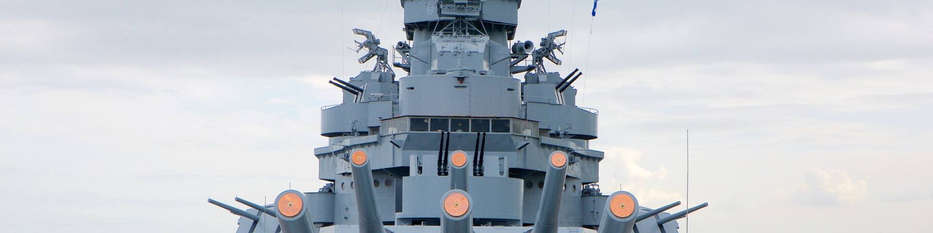 A large naval ship with multiple gun turrets and a flag.