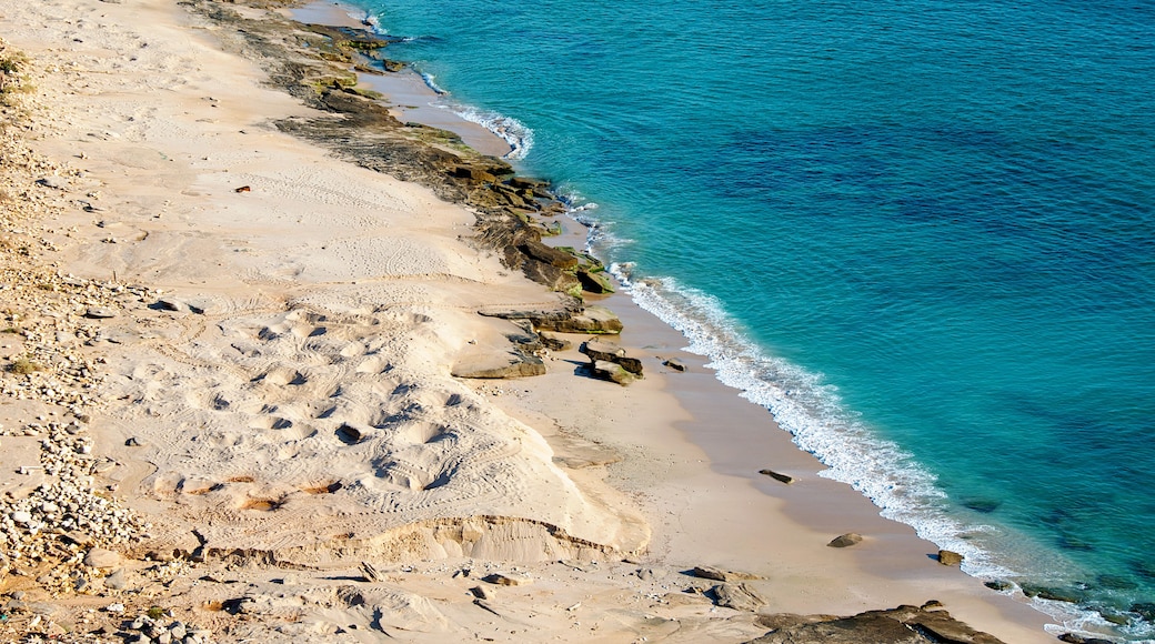 A sandy beach with clear blue water and rocky outcrops.