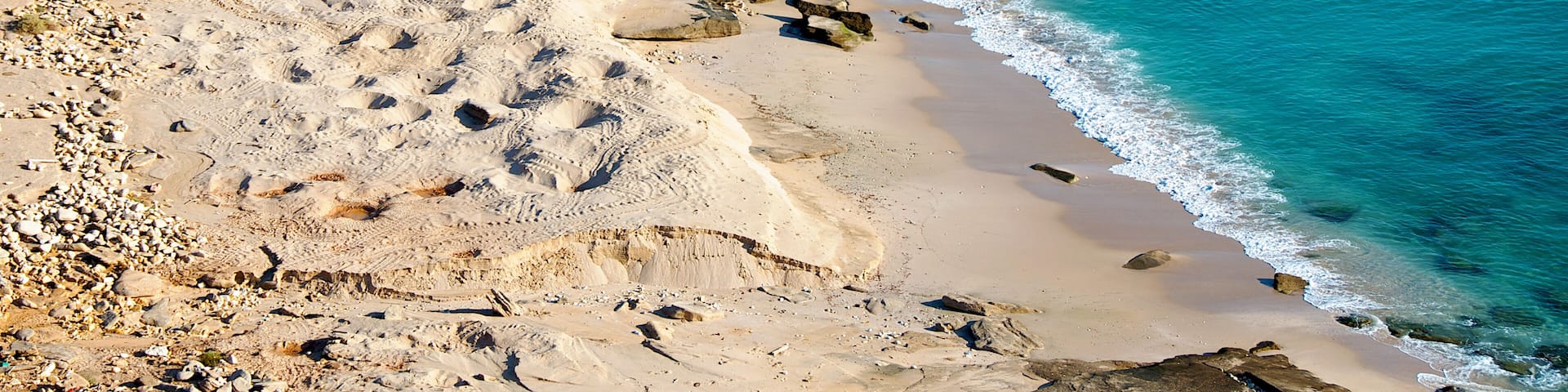 A sandy beach with clear blue water and rocky outcrops.