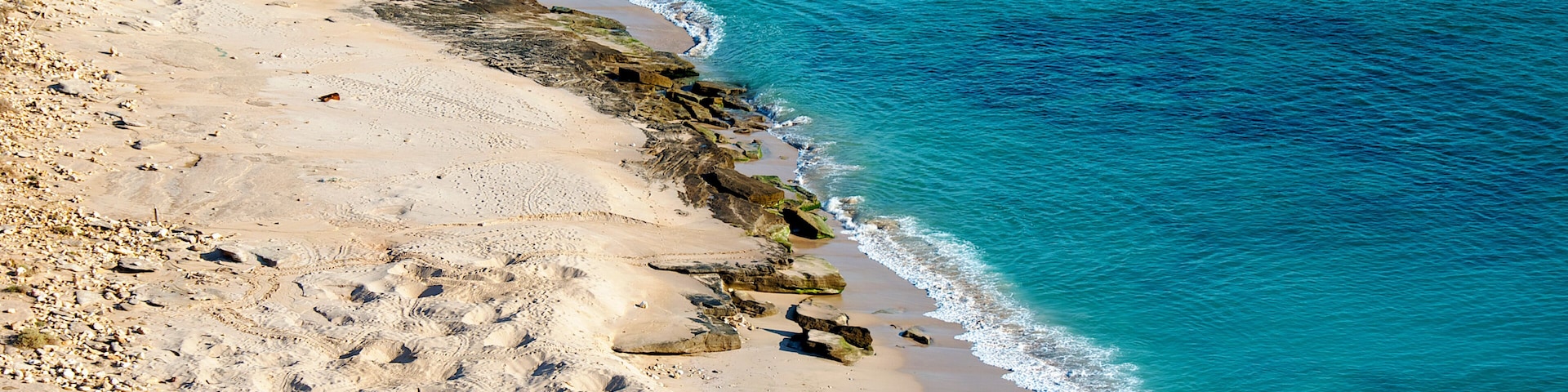 A sandy beach with clear blue water and rocky outcrops.