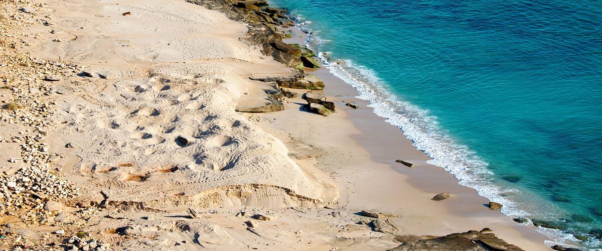 A sandy beach with clear blue water and rocky outcrops.
