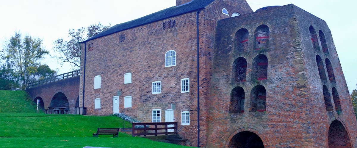 A large brick building with arched windows and a picnic table in a grassy area.