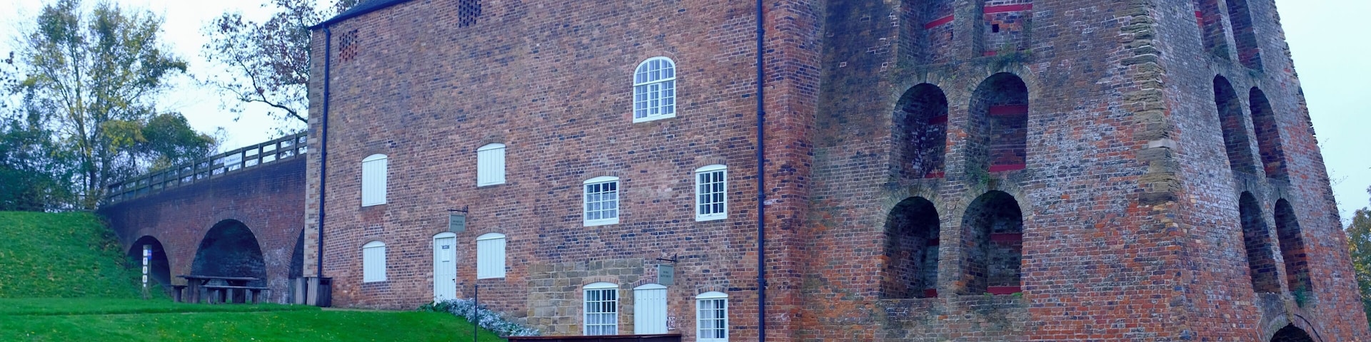 A large brick building with arched windows and a picnic table in a grassy area.