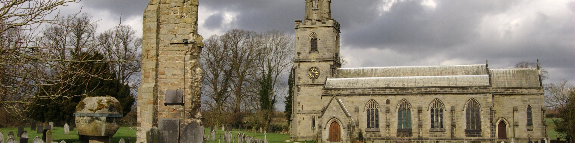 St George's parish church, Ticknall, Derbyshire, seen from the south. On the left in the foreground is the truncated Medieval churchyard cross. Centre left between the cross and St George's church is the ruin of the tower of the Medieval church of St Thomas Becket. St Thomas Becket's was demolished when St George's was built.