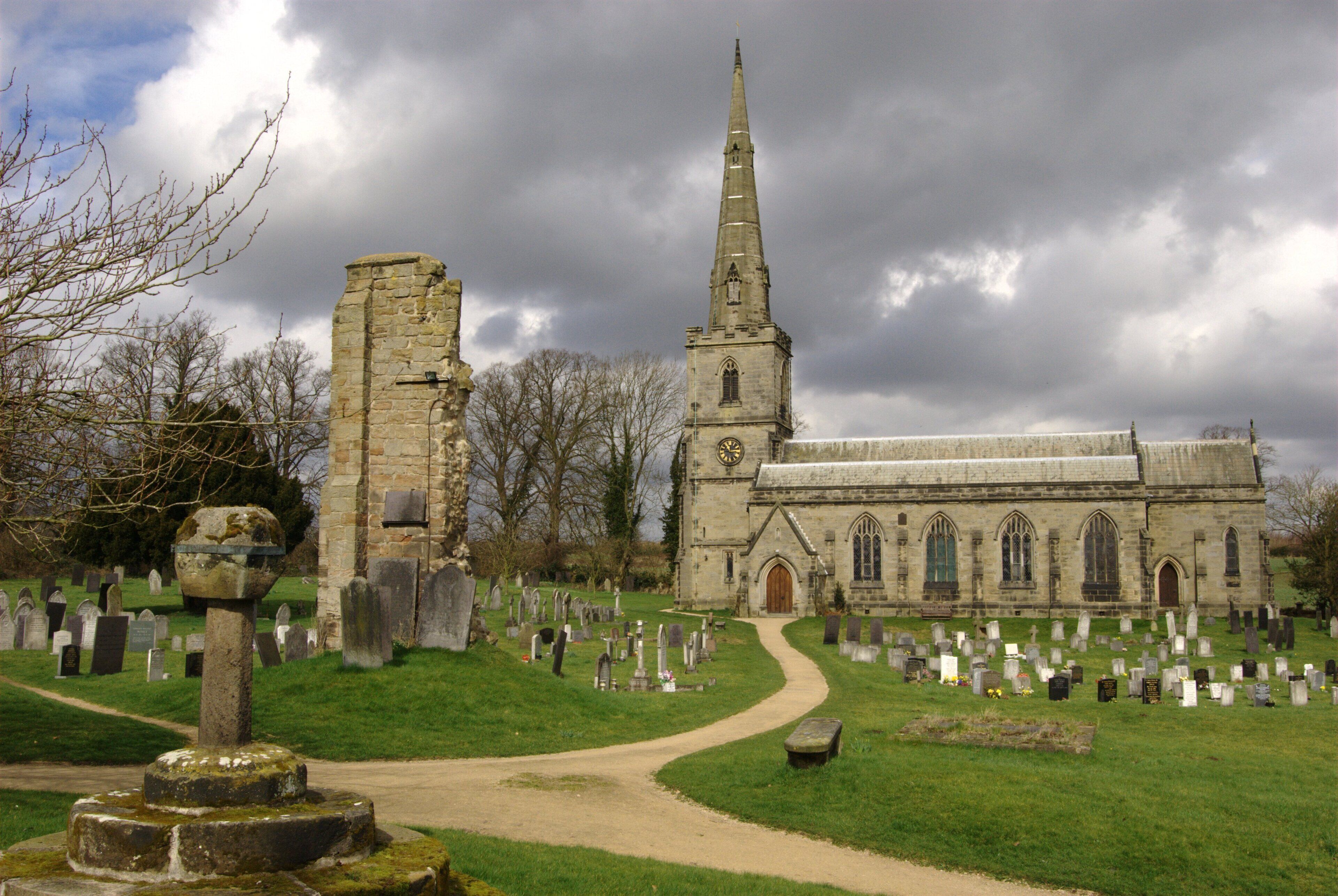A church with a tall spire and a graveyard with numerous headstones.