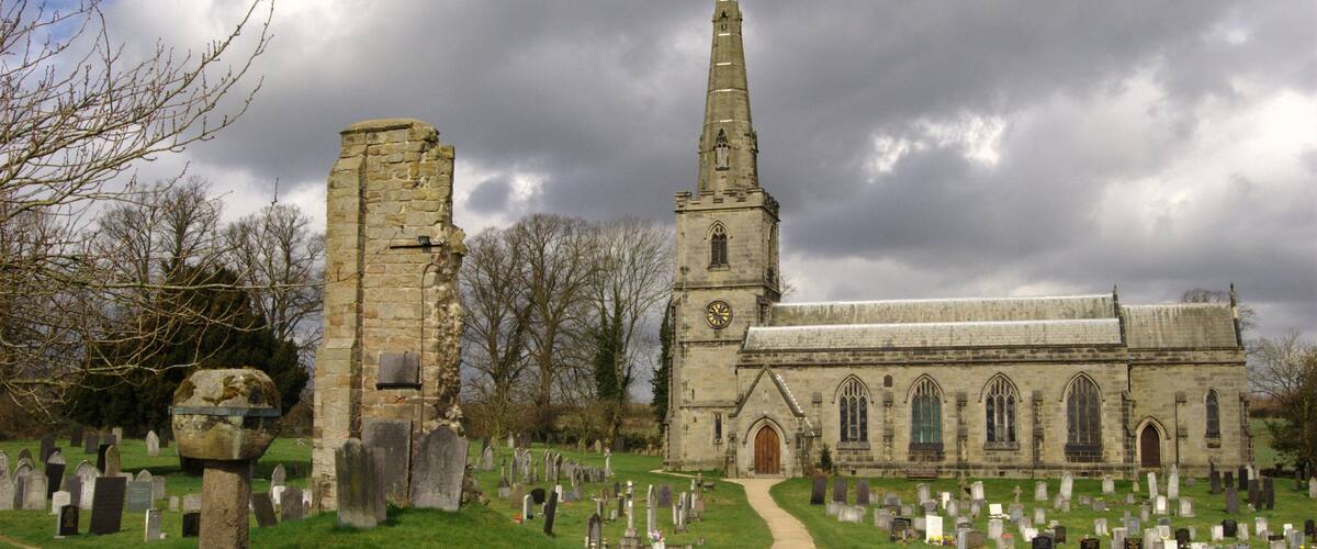 A church with a tall spire and a graveyard with numerous headstones.