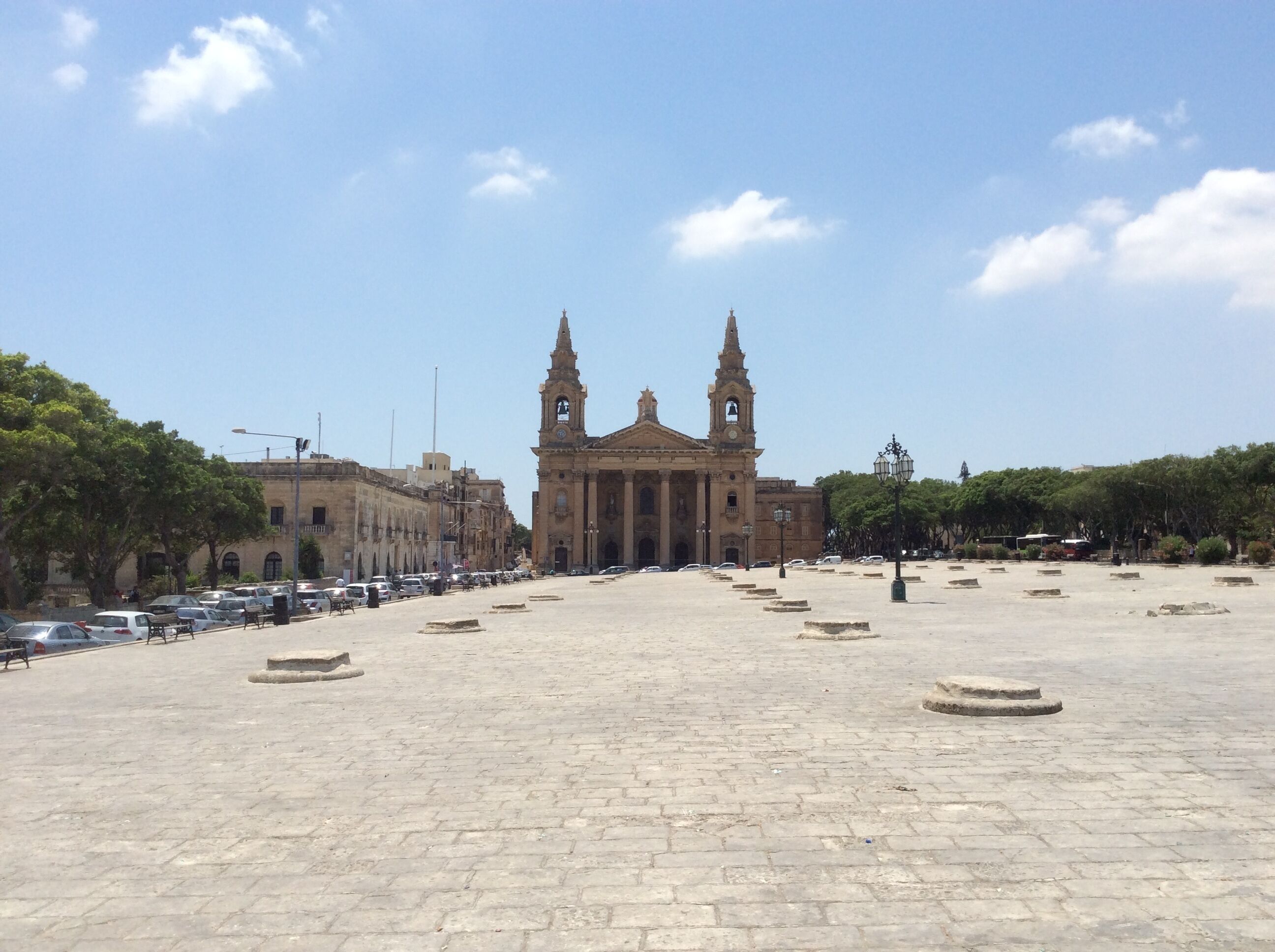 A plaza with a historic building featuring two towers and a clock.