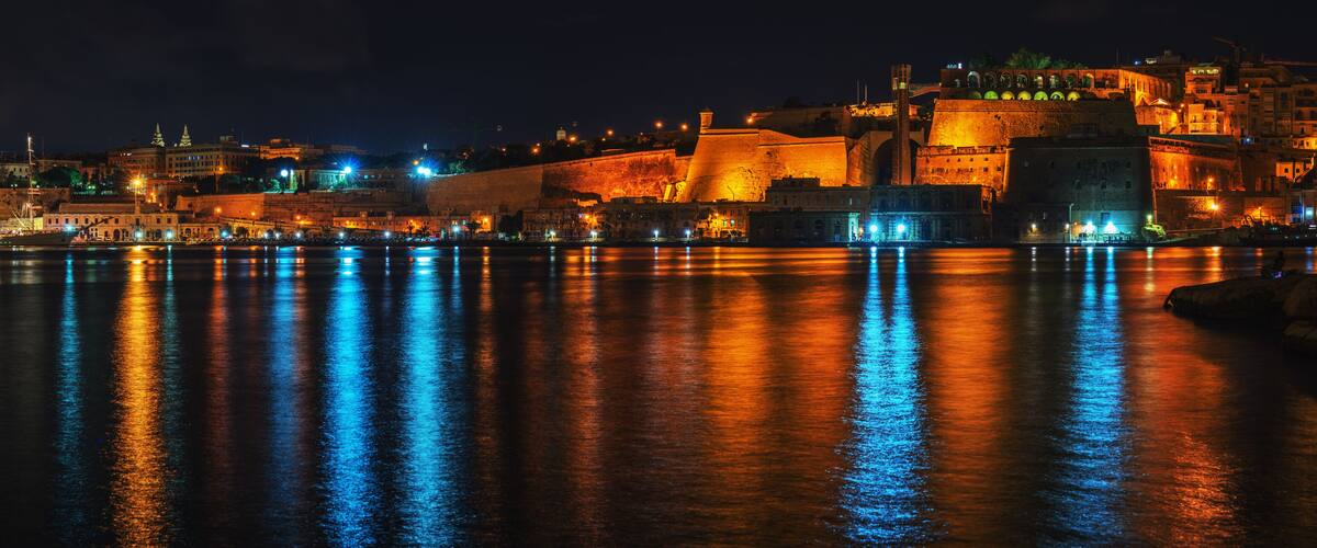 A nighttime cityscape with illuminated buildings reflecting on the water.