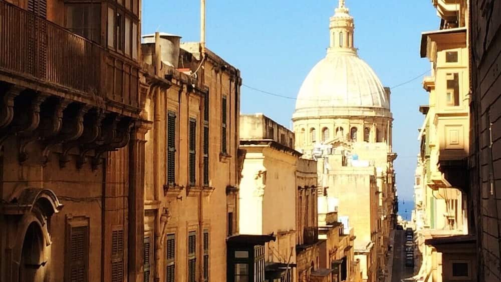 A narrow street with historic buildings and a prominent dome structure in the background.