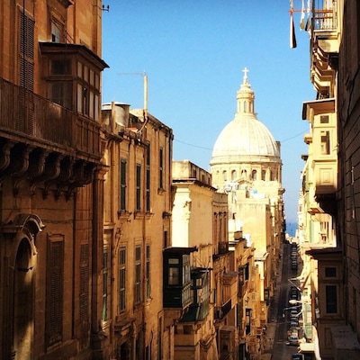 Una calle estrecha con edificios históricos y una estructura en forma de cúpula destacada al fondo.