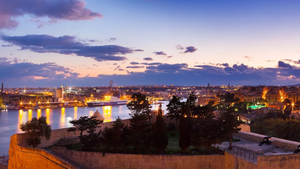 A cityscape at dusk with a river, illuminated buildings, and a historic fort.
