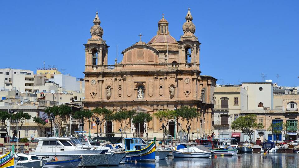 A historic church with two towers, surrounded by boats and buildings.