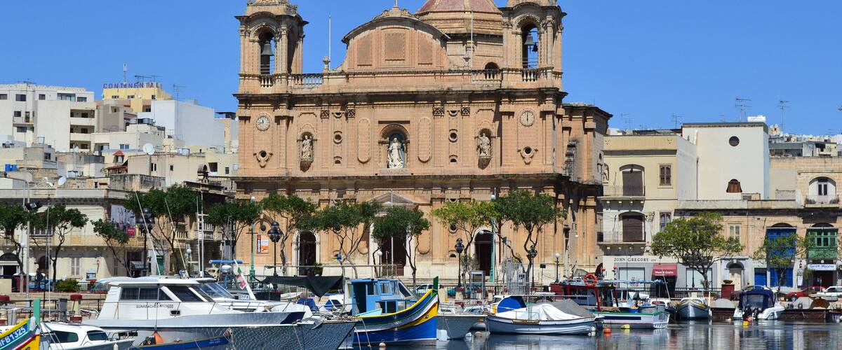 A historic church with two towers, surrounded by boats and buildings.