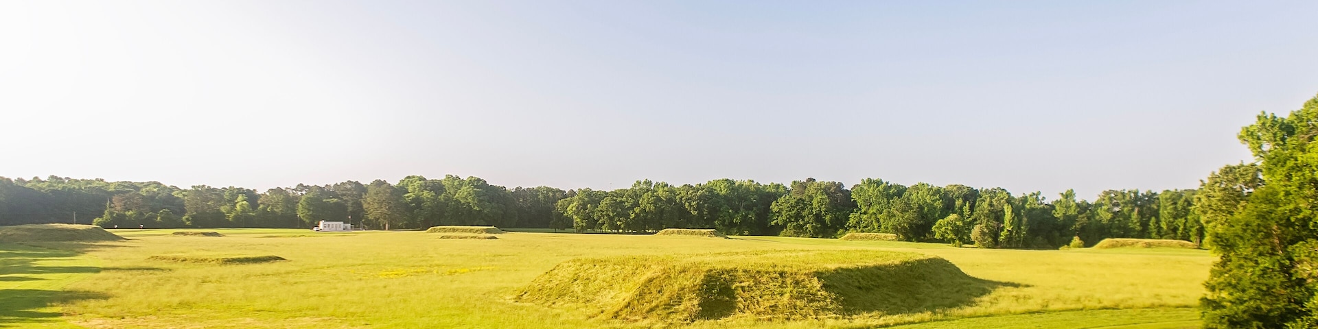 Un campo de golf con cielo despejado, césped verde y una carretera.