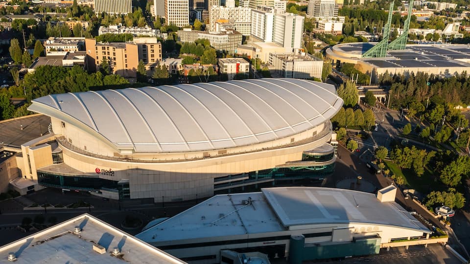 A large stadium with a distinctive curved roof, surrounded by urban buildings and greenery.