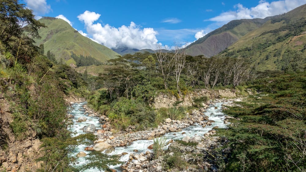 A river flowing through a mountainous valley with lush greenery and rocky terrain.