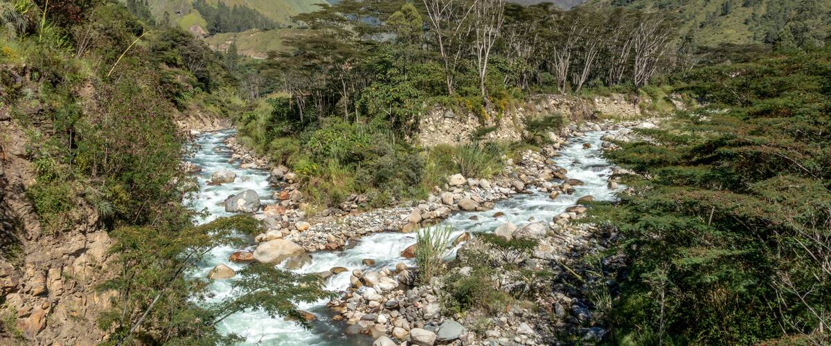 A river flowing through a mountainous valley with lush greenery and rocky terrain.