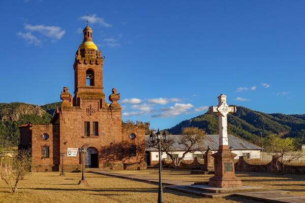 A historic church with a tall bell tower and a cross monument in a rural setting.