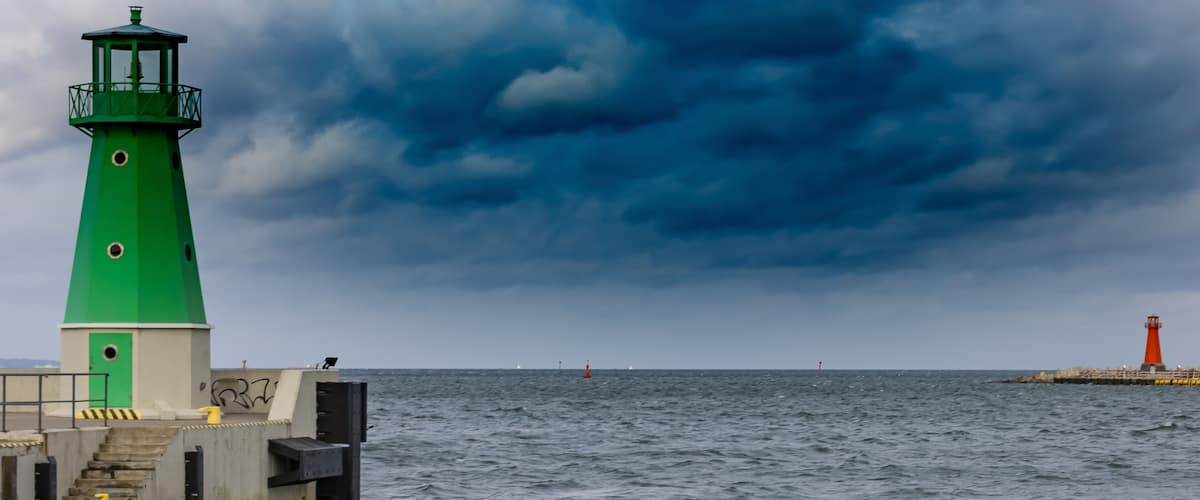 A green lighthouse on a pier with a red lighthouse in the distance.