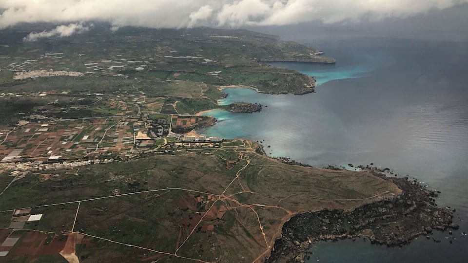 An aerial view of a coastal landscape with fields, a small town, and a clear blue sea.