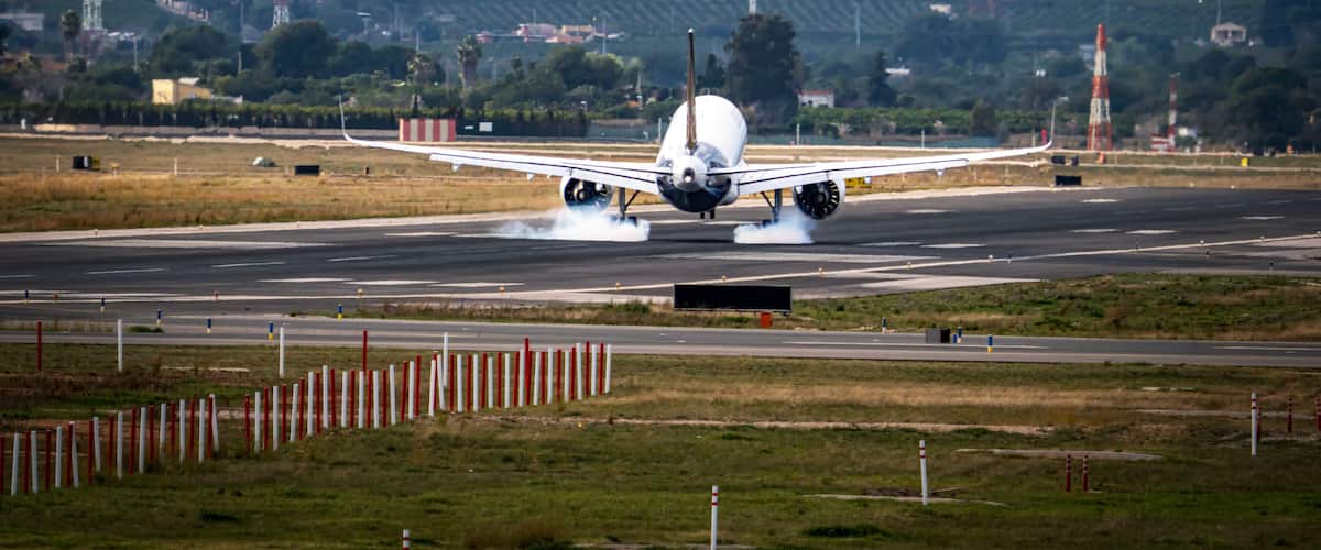 An airplane taking off with smoke from its tires, runway, and surrounding landscape with hills and buildings.