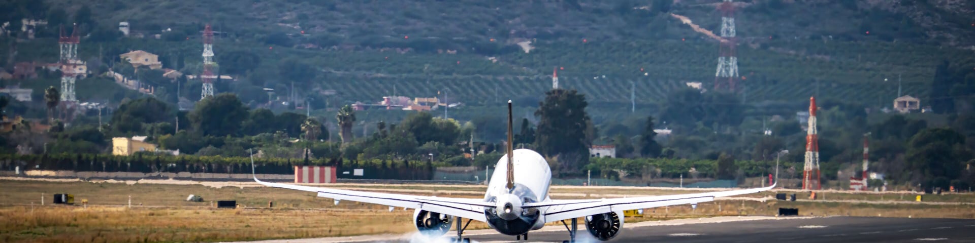 An airplane taking off with smoke from its tires, runway, and surrounding landscape with hills and buildings.