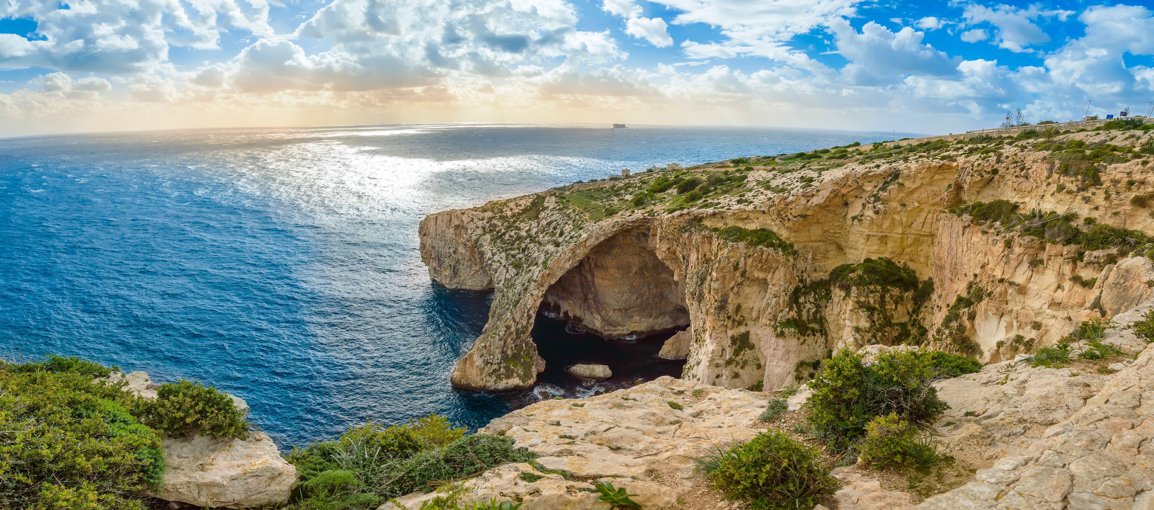 Un acantilado costero con la entrada natural a una cueva, con vista al mar.