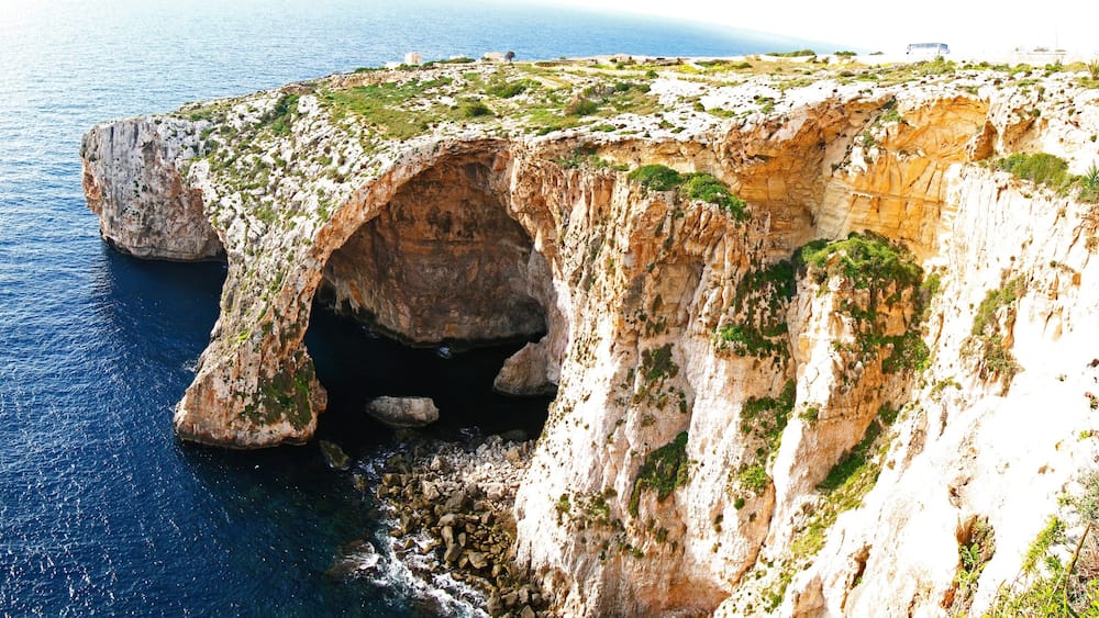 Eine Küstenklippe mit einer Höhle, felsigem Ufer und spärlicher Vegetation.