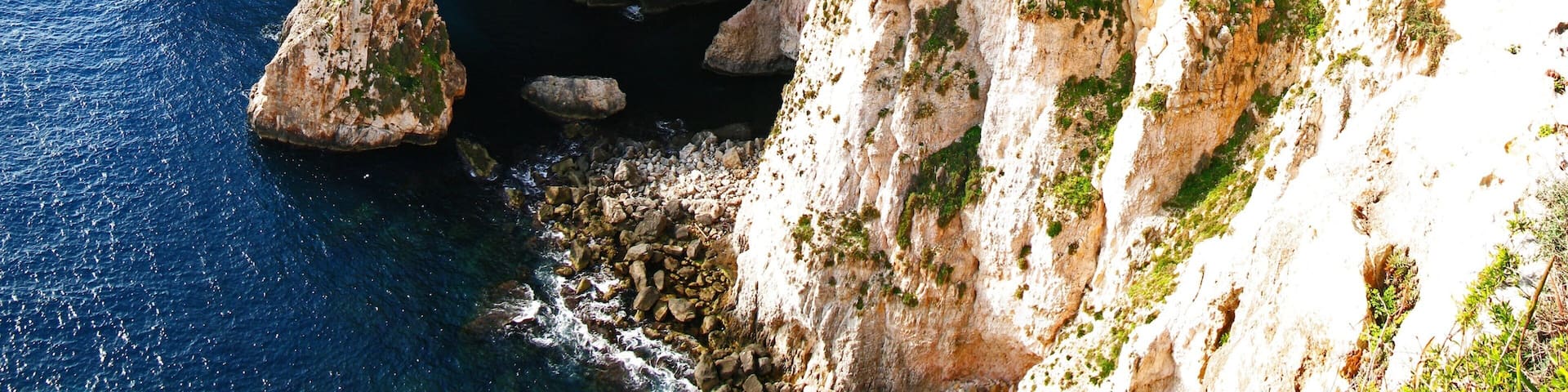 A coastal cliff with a cave entrance, rocky shoreline, and sparse vegetation.
