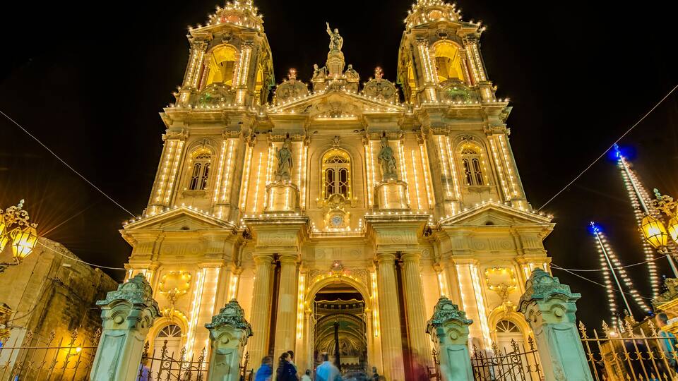 A grand, illuminated cathedral with ornate statues and a large central archway.