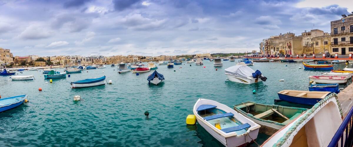 A harbor filled with small boats, a waterfront promenade, and historic buildings in the background.