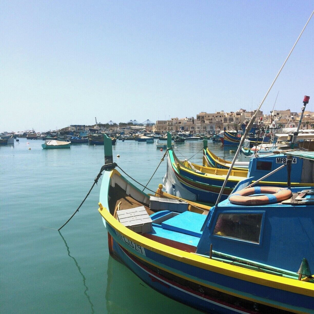 A harbor with several colorful boats docked, a lifebuoy, and buildings in the background.