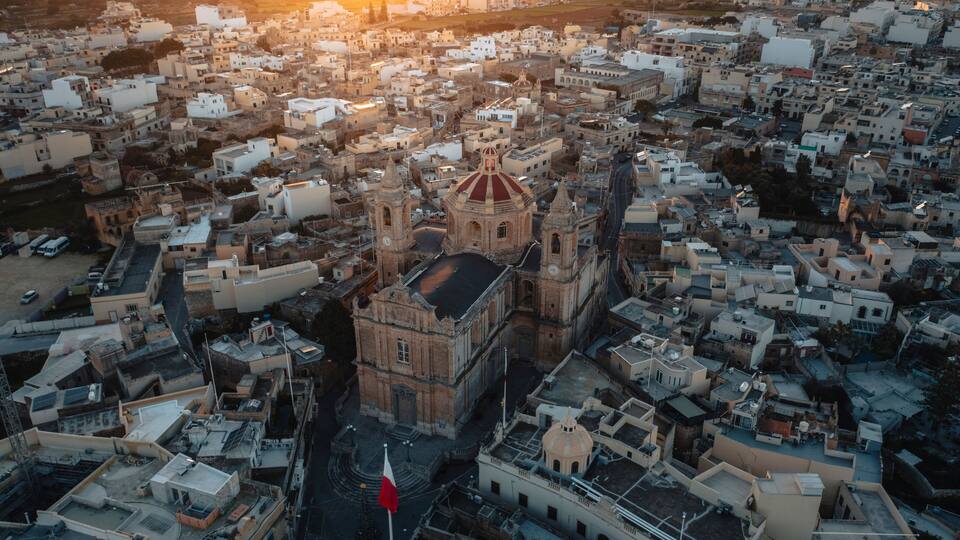 An aerial view of a densely packed urban area with a prominent historical building featuring a red dome and bell towers.