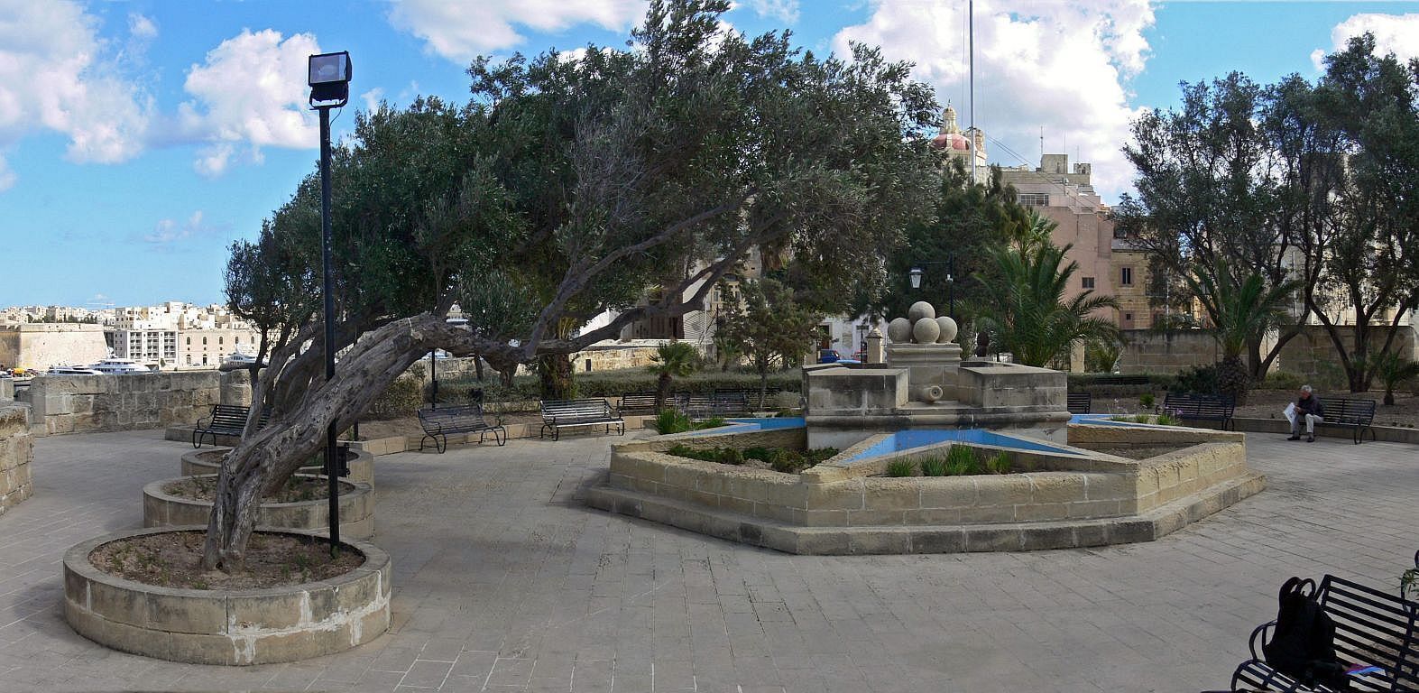 Una plaza pública con una fuente, bancos y árboles.