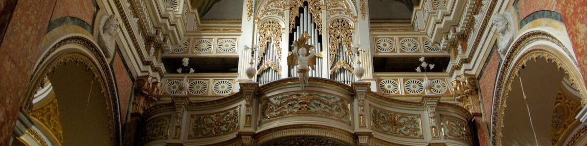 An ornate church interior with detailed gold and white decorations, a large organ, and a fresco on the ceiling.