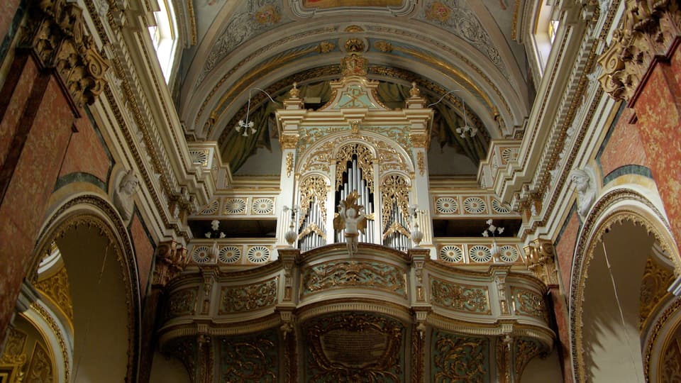 An ornate church interior with detailed gold and white decorations, a large organ, and a fresco on the ceiling.