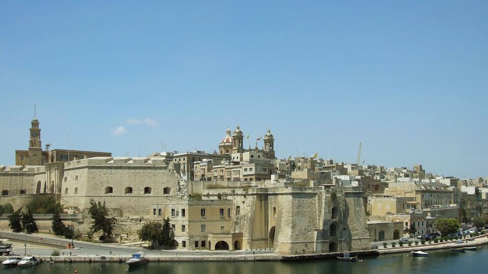 A coastal cityscape with historic buildings, a prominent clock tower, and a marina with boats.