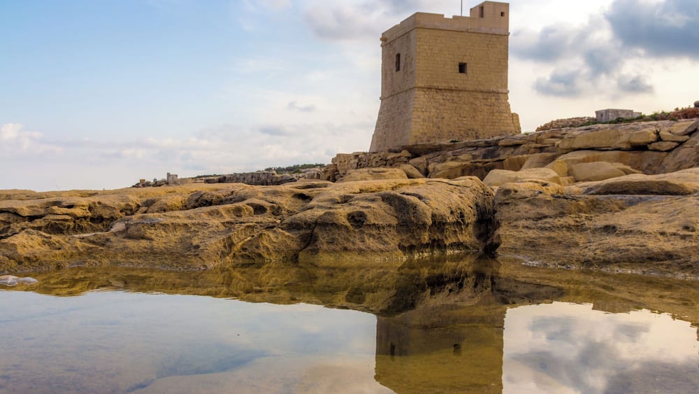 A stone tower on a rocky outcrop with a clear reflection in the water.