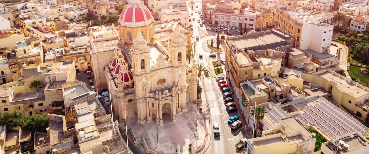 An aerial view of a city with a prominent cathedral featuring a large red dome, surrounded by urban buildings and streets.