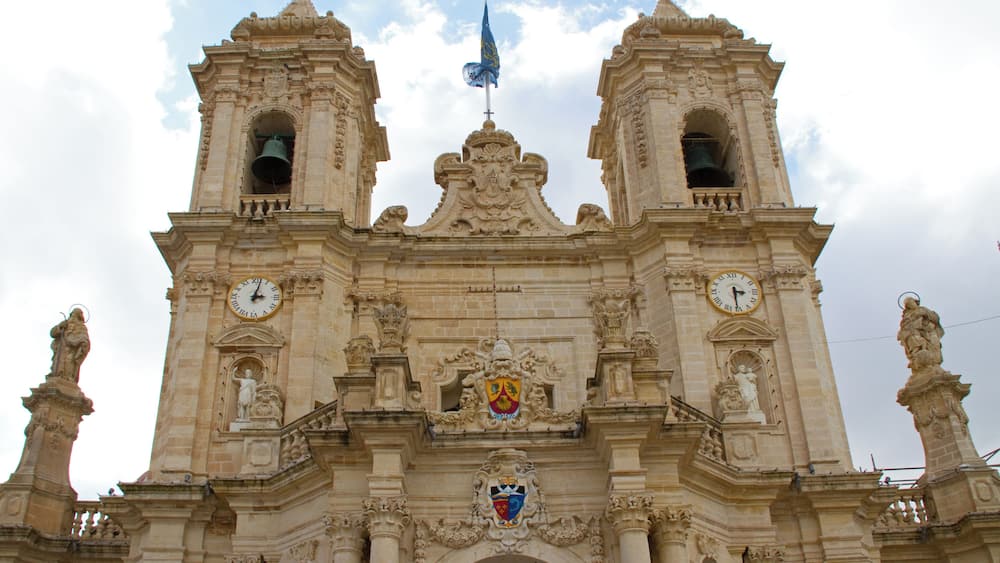 A historic building with two bell towers, a central archway, and a coat of arms.