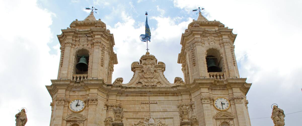 Un edificio histórico con dos torres de campanas, un arco central y un escudo de armas.