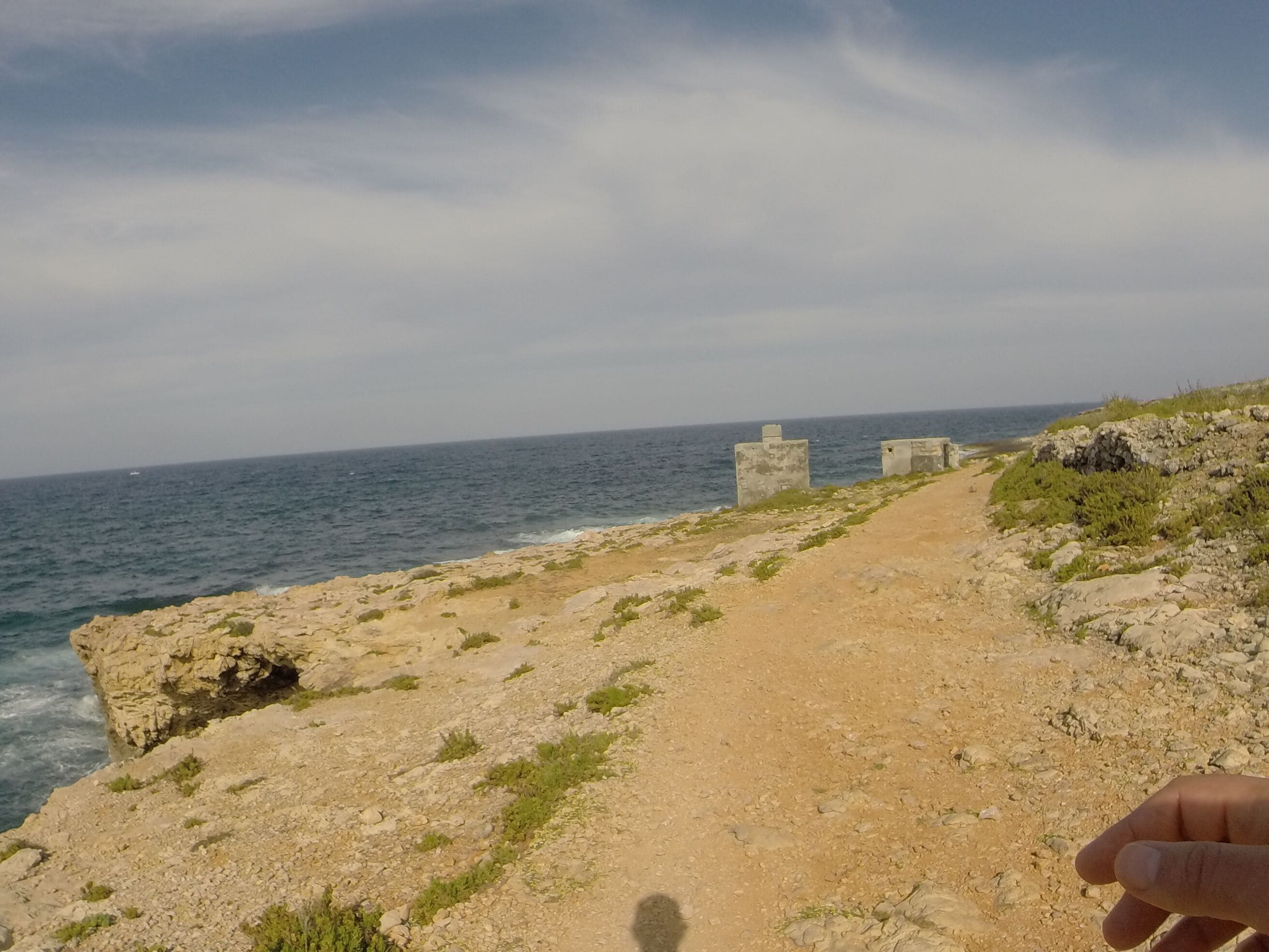 A rocky coastal path with the sea in the background and a clear sky.