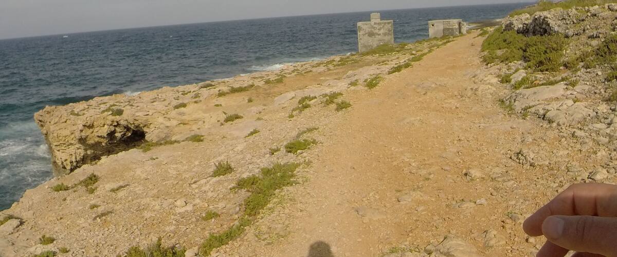 A rocky coastal path with the sea in the background and a clear sky.