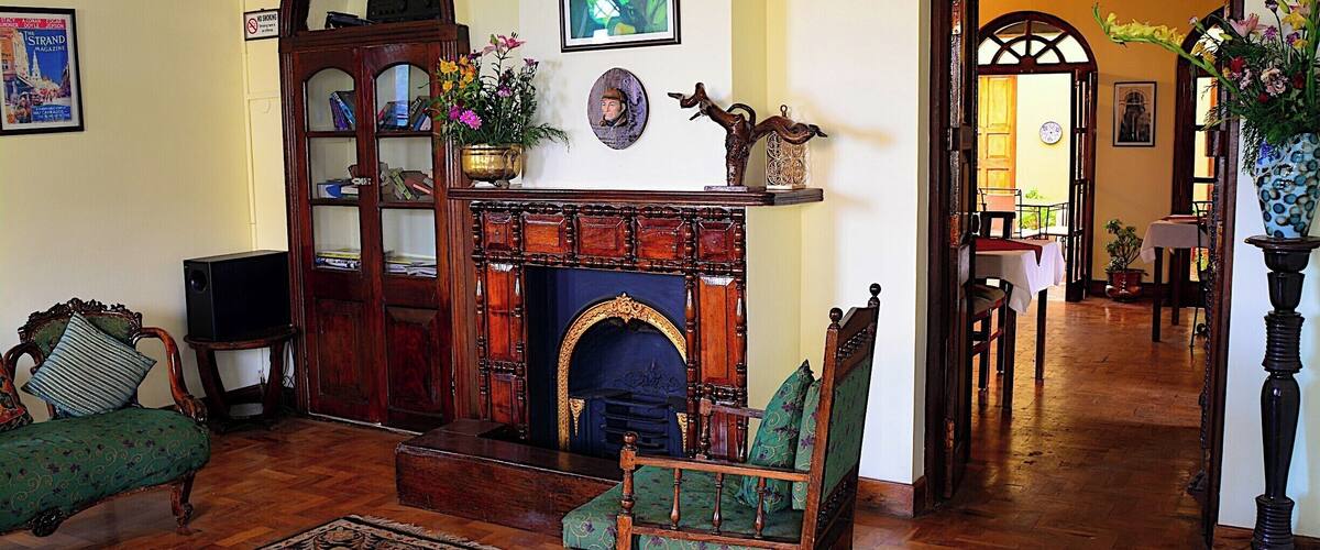 A traditional living room with a fireplace, green upholstered furniture, and a wooden cabinet.