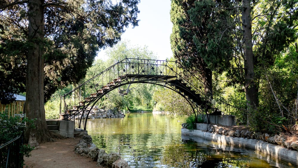 Un pont de pierre enjambant une rivière paisible, entouré d’arbres et bordé d’une promenade en bois.