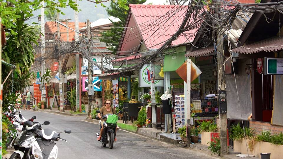 A street with motorcycles parked on the side, a person riding a motorcycle, and various shops with signs.