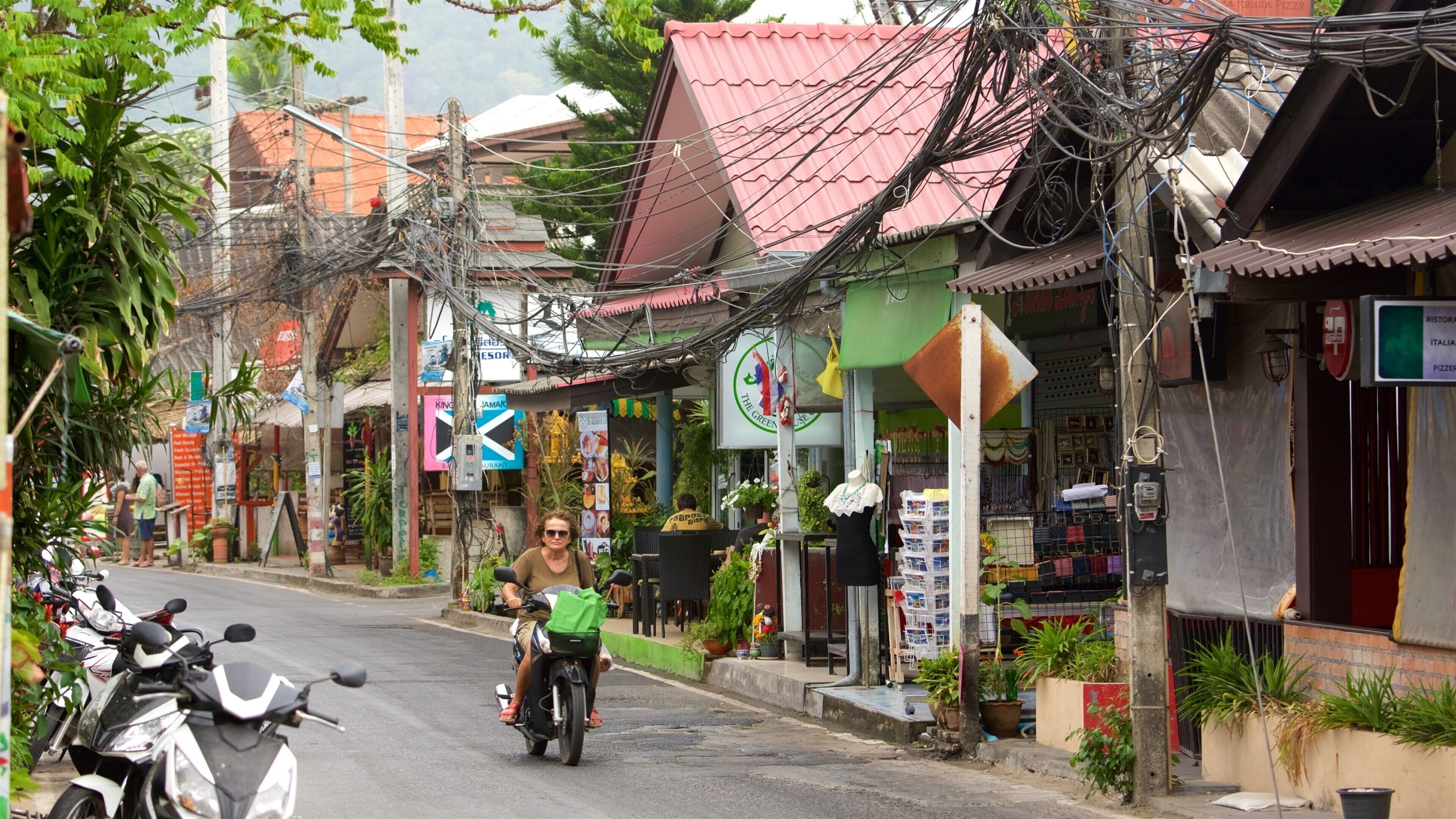 A street with motorcycles parked on the side, a person riding a motorcycle, and various shops with signs.